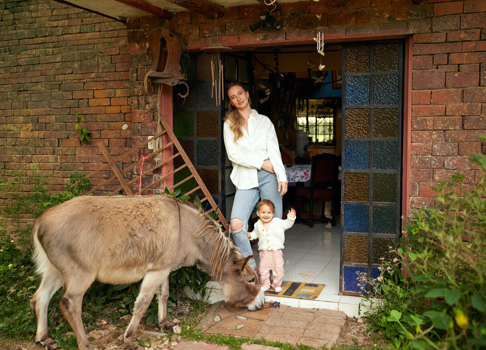 Sophia and her child in a doorway with a donkey grazing nearby