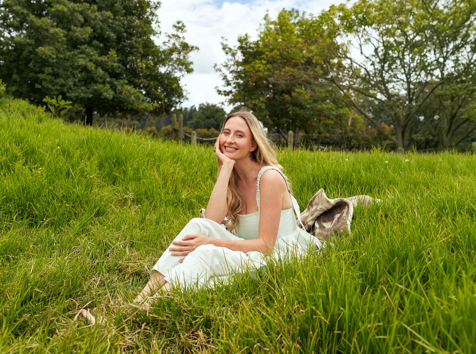 Sophia smiling, seated in long grass on a sunny day